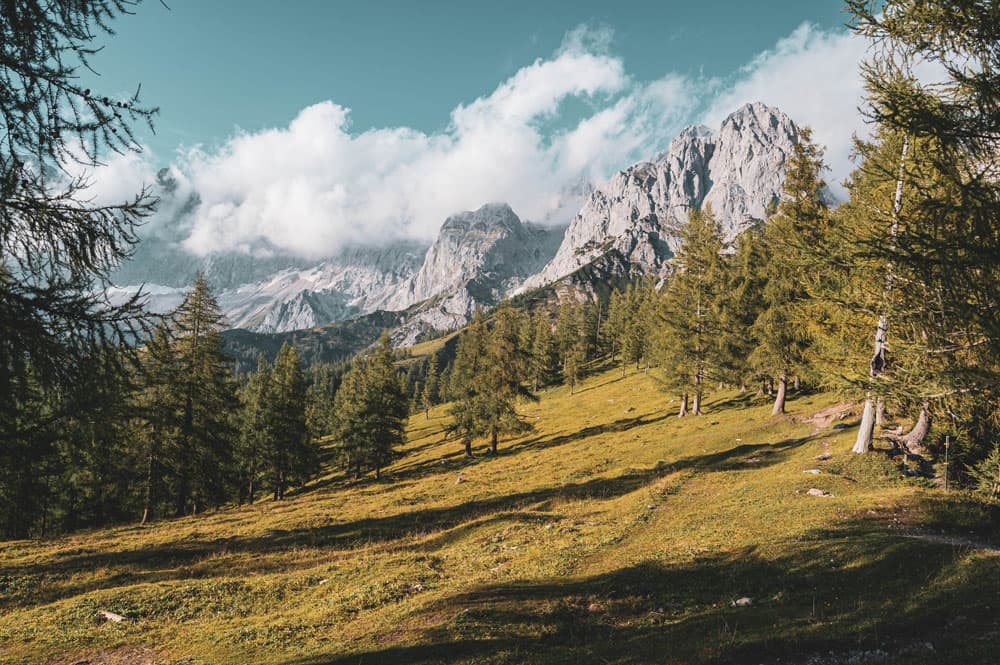 Ein Bild vom Dachstein im Sommer. Woken hängen über den Dachstein mit Wald und Wiesen