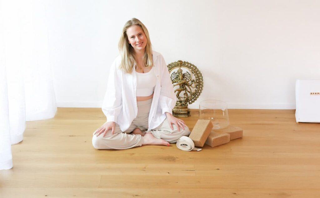 Frau sitz am Boden im Yoga Raum und bereitet sich auf den Yoga Kurs vor